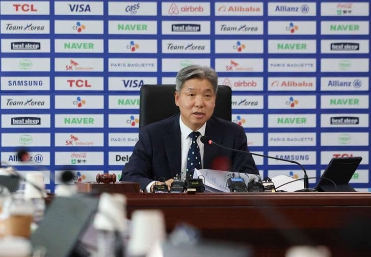 An official speaking at a Korea Sport and Olympic Committee press conference in front of a sponsor backdrop