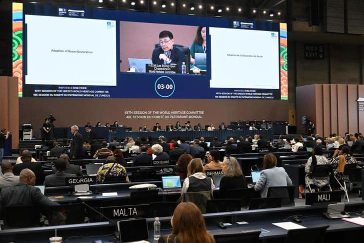 Delegates seated in the plenary hall of the 48th session of the UNESCO World Heritage Committee in Busan, with screens overhead reading Adoption of Busan Declaration